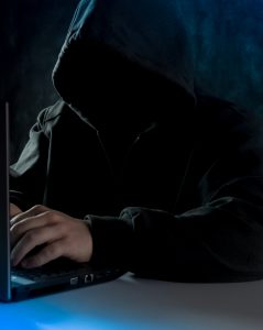 Anonymous computer hacker in hoodie. Using laptop computer for cyber attack and calling on cellphone.